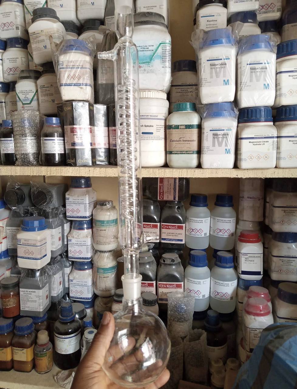 Shelves of laboratory chemicals with a condenser and round-bottom flask